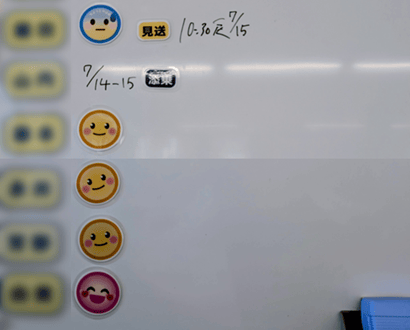 ホワイトボードにメンバー毎に毎朝顔文字マグネットを貼っている写真